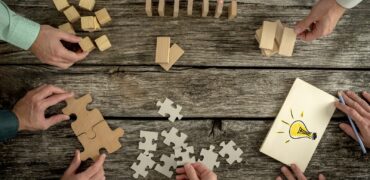 Businessmen planning business strategy while holding puzzle pieces, creating ideas with light bulb drawn on paper and rearranging wooden blocks. Conceptual of teamwork, strategy, vision or education.